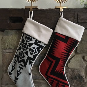 May include: Two Christmas stockings with geometric patterns. One stocking is white with black geometric designs, and the other is red with black geometric designs. Both stockings have white cuffs and are hanging from gold star-shaped hooks.