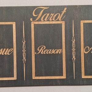 Puede incluir: Un tablero de lectura de tarot de madera con tres ranuras para cartas. Las ranuras est&aacute;n etiquetadas como "Problema", "Raz&oacute;n" y "Acci&oacute;n". El tablero est&aacute; decorado con un s&iacute;mbolo de triple luna, estrellas y dise&ntilde;os florales.