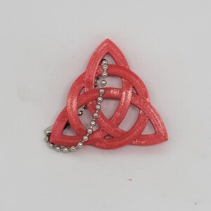 Puede incluir: Un colgante de nudo celta rojo tridimensional con una cadena plateada.