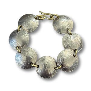 May include: A silver coin bracelet featuring eight connected quarters. The quarters are linked with gold-colored metal rings and a clasp. The coins display various designs and text, including "United States of America."