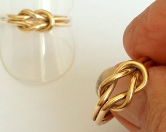 Puede incluir: Un anillo de oro con un diseño de nudo. El anillo está hecho de una sola pieza de metal y está pulido a un alto brillo.