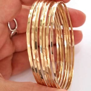 May include: A set of ten gold-toned hammered metal bangles. The bangles are stacked on top of each other and are all the same width.