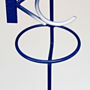 May include: A blue metal stand with two circular rings and a white and blue "KC" logo. The stand is designed to hold items such as glasses or bottles.