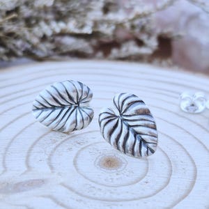 Peut inclure: Une paire de boucles d'oreilles à clous en argent en forme de feuilles en cœur avec des nervures en relief détaillées et une finition polie. Les boucles d'oreilles présentent une pointe arrondie et incluent deux petits fermoirs papillon.
