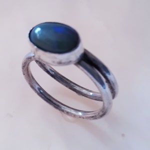 Könnte beinhalten: Ein silberner Ring mit einem dunkelblauen ovalen Edelstein. Der Ring ist doppelt gefasst und hat ein schlichtes Design.