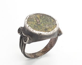 May include: A silver ring with a green stone set in a circular bezel. The ring has a scroll design on the band.