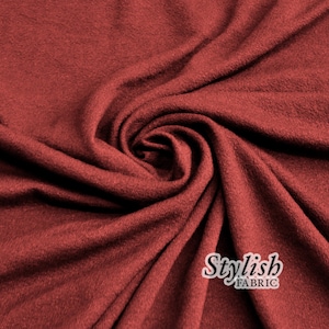 Könnte beinhalten: Nahaufnahme eines gewirbelten, strukturierten Stoffes in einem tiefen Rotbraun. Der Stoff hat ein weiches, drapiertes Aussehen mit sichtbaren Falten und subtilen Schatten. Die Worte "Stylish FABRIC" sind in weißer Schrift gedruckt.