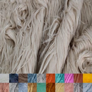 May include: A close-up of a beige faux fur fabric. The fabric has a long, shaggy pile and a soft, fluffy texture. The fabric is perfect for crafting projects, such as making blankets, pillows, and clothing.