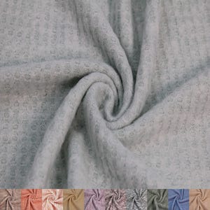 May include: A close-up of a soft, gray waffle knit fabric. The fabric is textured and has a slightly bumpy surface.