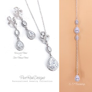 May include: Elegant silver-toned jewelry set featuring a necklace, earrings, and a backdrop necklace. The earrings and necklace have a floral design with teardrop-shaped clear stones. The backdrop necklace is 6.5 inches long. The jewelry is from the Pure Rain Designs Personalized Jewelry Collection.