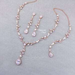 May include: Rose gold bridal jewelry set with a delicate vine design featuring clear crystals and pearls. The necklace has a long pendant with a teardrop crystal. The earrings are drop earrings with a teardrop crystal.