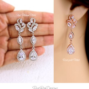 May include: Elegant silver platinum plated and rose gold plated drop earrings. The earrings feature a floral design with clear, sparkling crystals and a teardrop-shaped stone at the bottom. The earrings are part of the Pure Rain Designs Personalized Jewelry Collection.