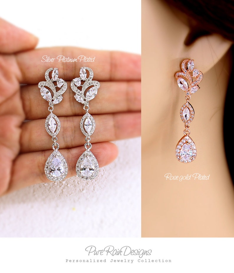 May include: Elegant silver platinum plated and rose gold plated drop earrings. The earrings feature a floral design with clear, sparkling crystals and a teardrop-shaped stone at the bottom. The earrings are part of the Pure Rain Designs Personalized Jewelry Collection.