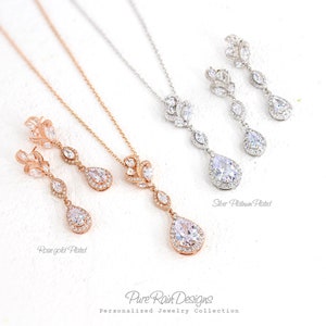 May include: Elegant jewelry sets featuring necklaces and matching earrings. The sets are available in rose gold and silver platinum plating. Each set includes a pendant necklace with a teardrop-shaped pendant and matching drop earrings. The jewelry is from Pure Rain Designs.