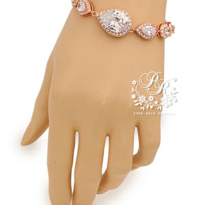 K&ouml;nnte beinhalten: Rosenvergoldetes Armband mit einem gro&szlig;en, klaren, birnenf&ouml;rmigen Kristall, der von kleineren Kristallen umgeben ist. Das Armband befindet sich an einer Mannequin-Hand.