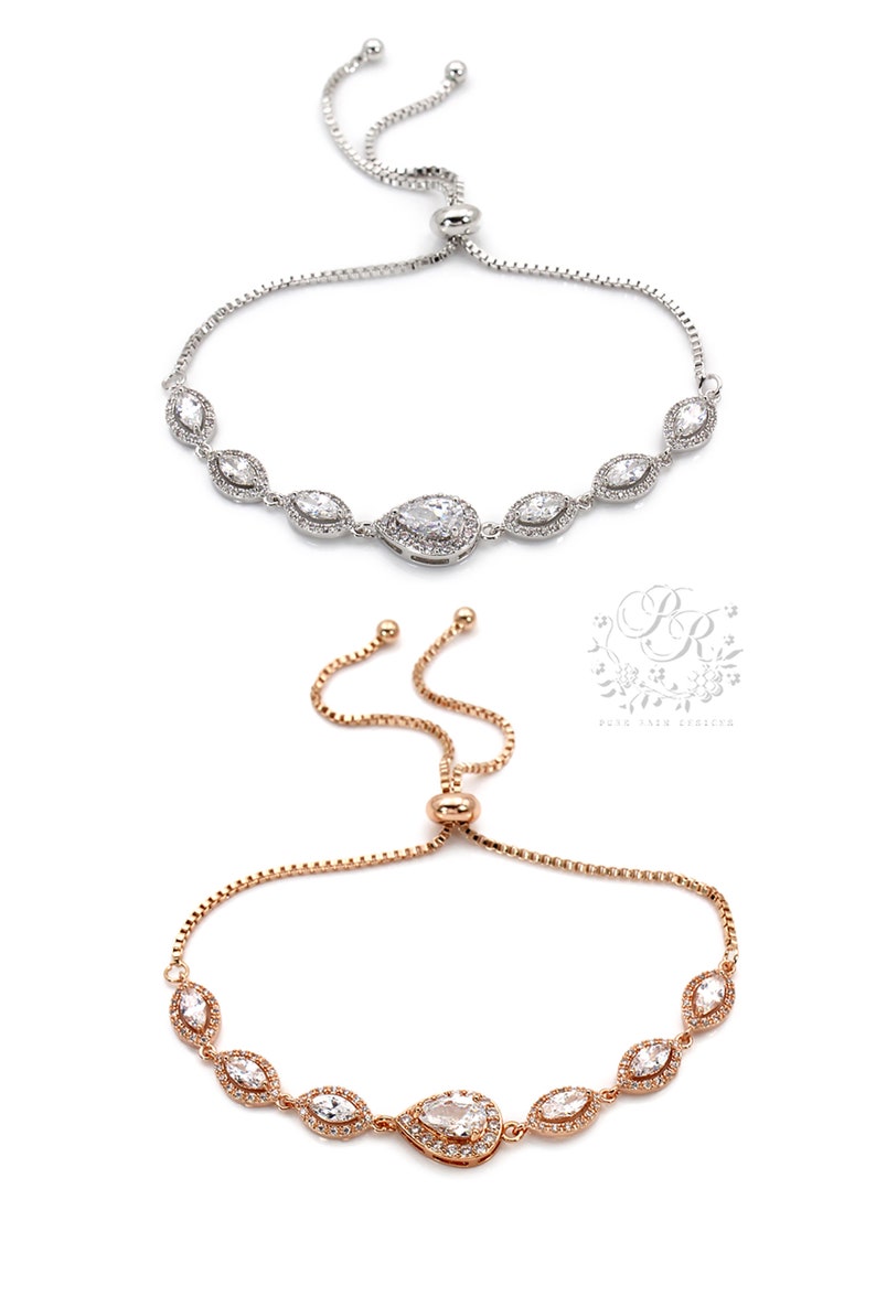May include: Two adjustable bracelets. The top bracelet is silver-toned, and the bottom bracelet is rose gold-toned. Both bracelets feature a series of clear, sparkling stones in a marquise and pear shape. The bracelets are on a white background.