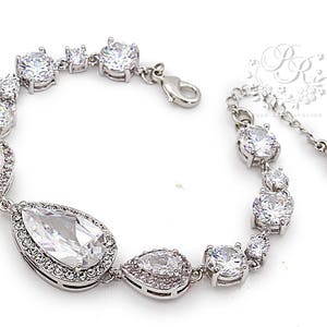 May include: A silver bracelet with a teardrop-shaped crystal pendant and smaller round crystals. The bracelet has a clasp closure.