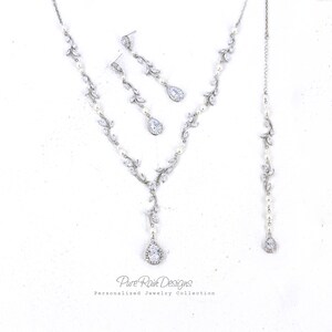 May include: A silver bridal jewelry set with a teardrop pendant necklace, matching earrings, and a pearl and crystal bracelet. The necklace features a delicate vine design with clear crystals and pearls.