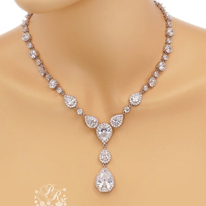 May include: A silver necklace with a teardrop pendant, featuring a large pear-shaped crystal surrounded by smaller crystals. The necklace is made of silver and has a delicate chain.