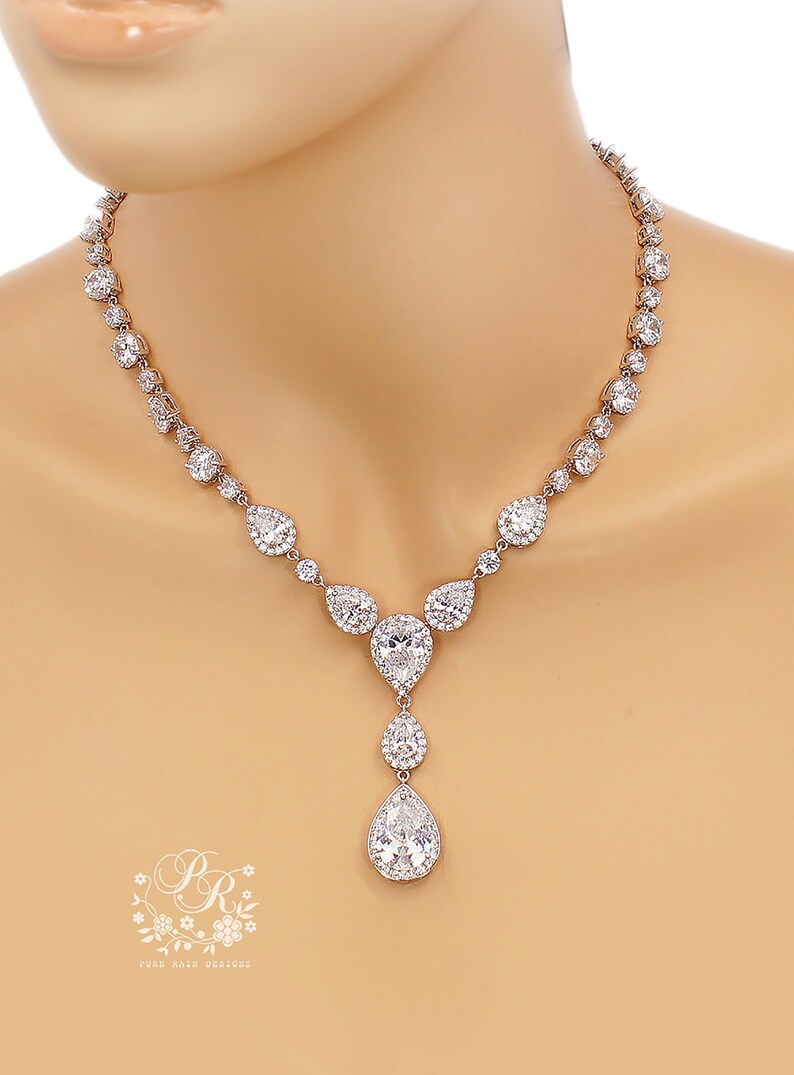 May include: A silver necklace with a teardrop pendant, featuring a large pear-shaped crystal surrounded by smaller crystals. The necklace is made of silver and has a delicate chain.