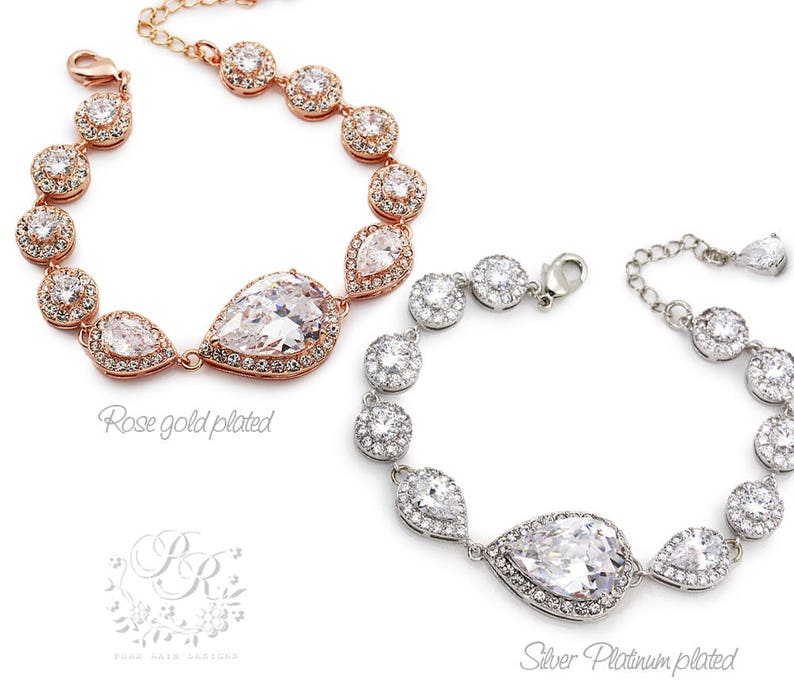 K&ouml;nnte beinhalten: Zwei Kristall-Brautarmreifen mit tropfenf&ouml;rmigen Mittelsteinen. Ein Armband ist ros&eacute;vergoldet und das andere ist silberplatiniert.