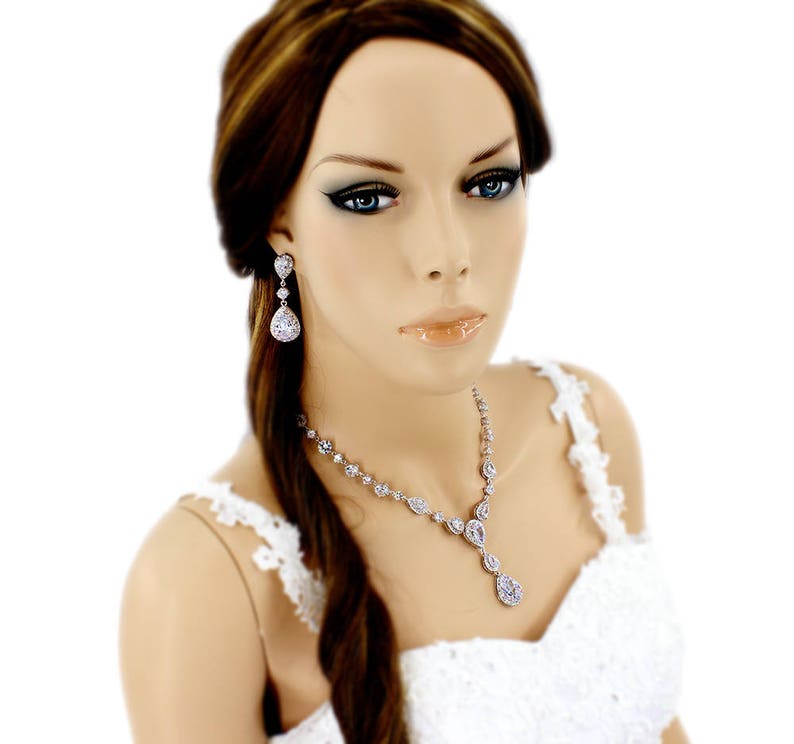 May include: A bridal jewelry set with a teardrop-shaped necklace and matching earrings. The set is made of silver and features clear cubic zirconia stones.