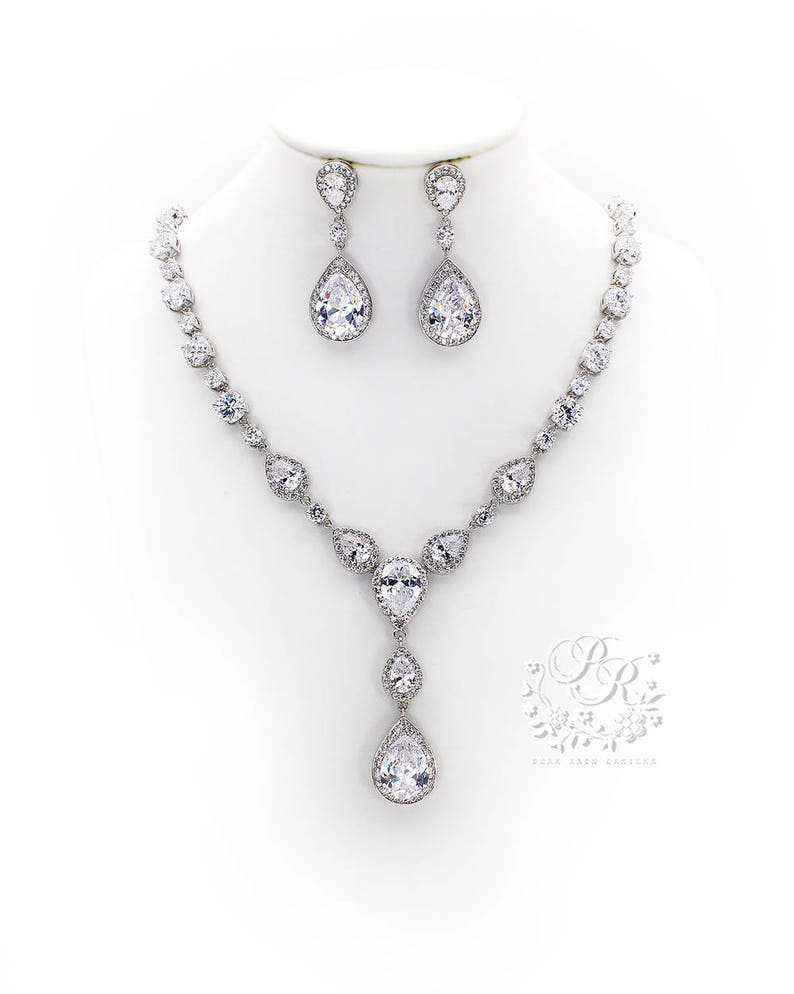 May include: A silver necklace and earrings set with teardrop-shaped clear crystals. The necklace has a long pendant with a large teardrop crystal.