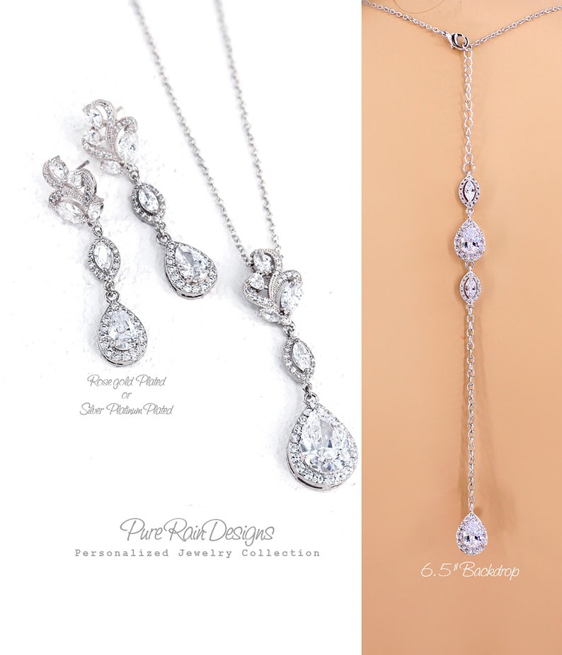 May include: Elegant silver-toned jewelry set featuring a necklace, earrings, and a backdrop necklace. The earrings and necklace have a floral design with teardrop-shaped clear stones. The backdrop necklace is 6.5 inches long. The jewelry is from the Pure Rain Designs Personalized Jewelry Collection.