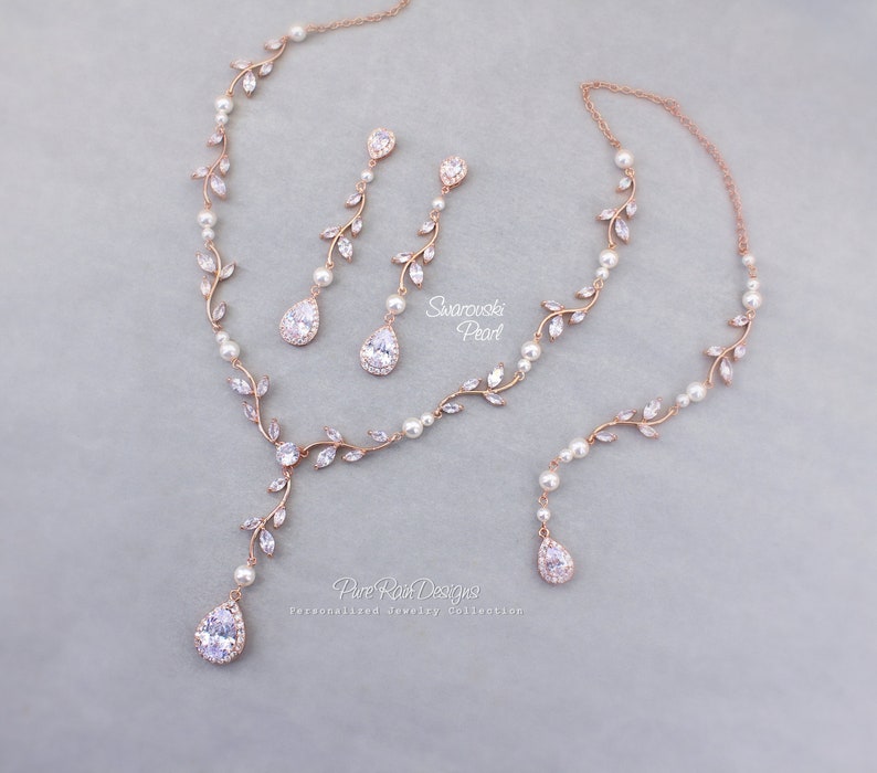 May include: Rose gold bridal jewelry set with a delicate vine design featuring clear crystals and pearls. The necklace has a long pendant with a teardrop crystal. The earrings are drop earrings with a teardrop crystal.