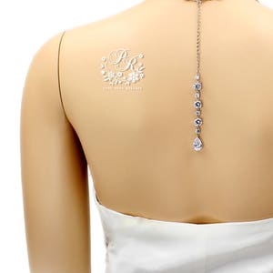 May include: A white bridal back necklace with a teardrop pendant and a small floral design with the initials "BR" on the back of a mannequin.