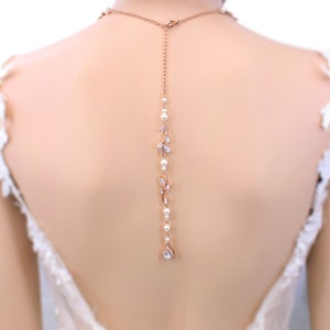 May include: A rose gold back necklace with a delicate design of leaves and pearls. The necklace has a teardrop-shaped crystal at the end.