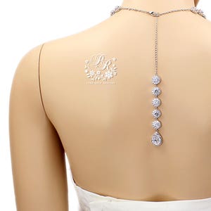 K&ouml;nnte beinhalten: Eine silberne R&uuml;ckenkette mit einem Tropfenanh&auml;nger und runden Steinen. Die Kette befindet sich an einem wei&szlig;en Mannequin.