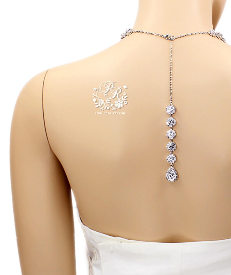 K&ouml;nnte beinhalten: Eine silberne R&uuml;ckenkette mit einem Tropfenanh&auml;nger und runden Steinen. Die Kette befindet sich an einem wei&szlig;en Mannequin.