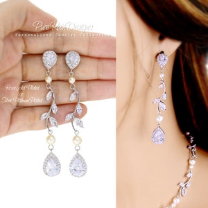 May include: A pair of silver teardrop earrings with a delicate vine design and pearl accents. The earrings are accented with clear cubic zirconia stones.