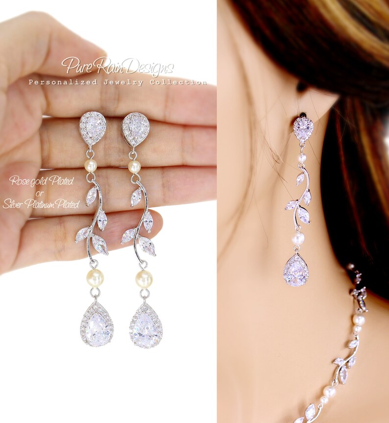 May include: A pair of silver teardrop earrings with a delicate vine design and pearl accents. The earrings are accented with clear cubic zirconia stones.