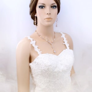 May include: A bride wearing a white lace wedding dress with a rose gold necklace and earrings. The necklace features a teardrop pendant.