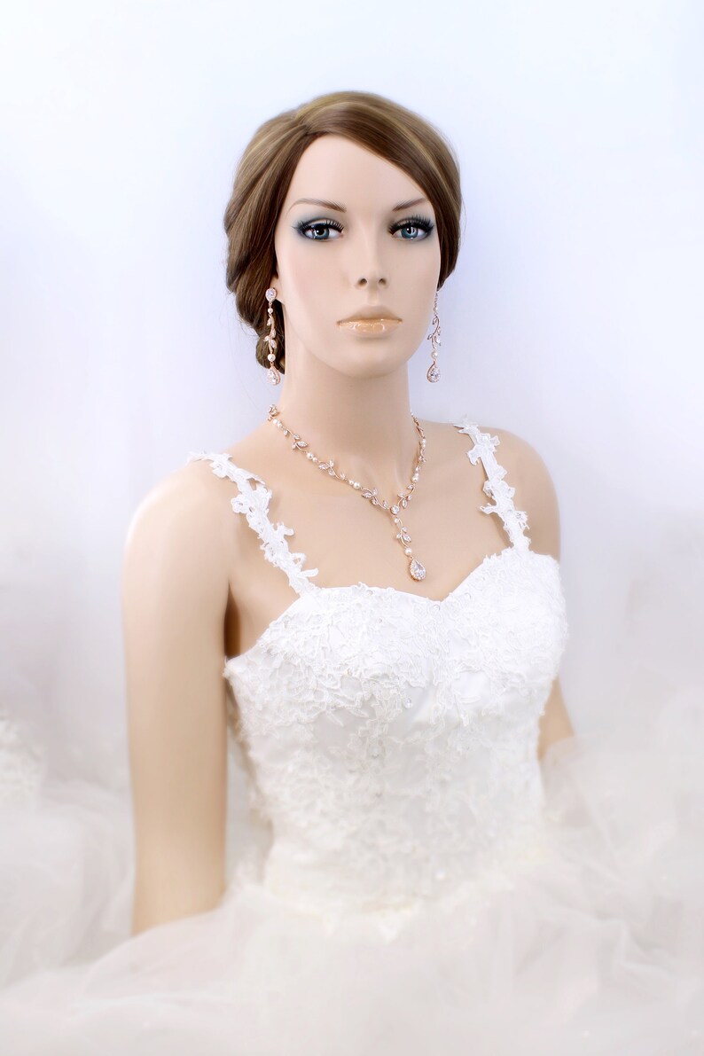 May include: A bride wearing a white lace wedding dress with a rose gold necklace and earrings. The necklace features a teardrop pendant.