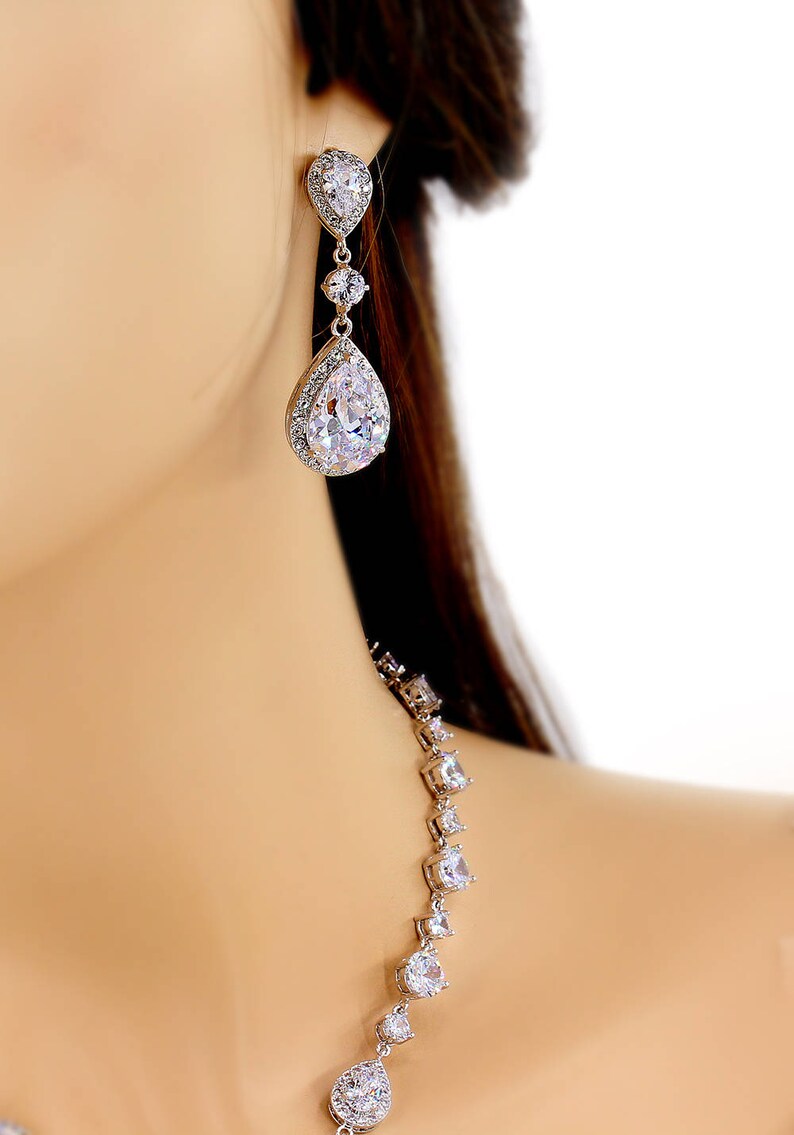 May include: A silver necklace and earrings set with teardrop-shaped cubic zirconia stones. The necklace has a long, delicate chain with a single teardrop stone at the bottom.
