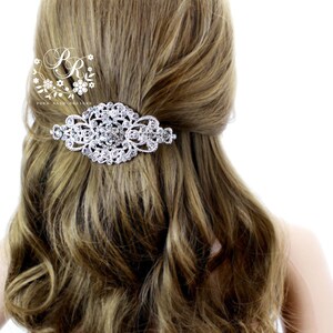 May include: A silver hair comb with a large, ornate design featuring clear rhinestones. The comb is shown in a model's hair.