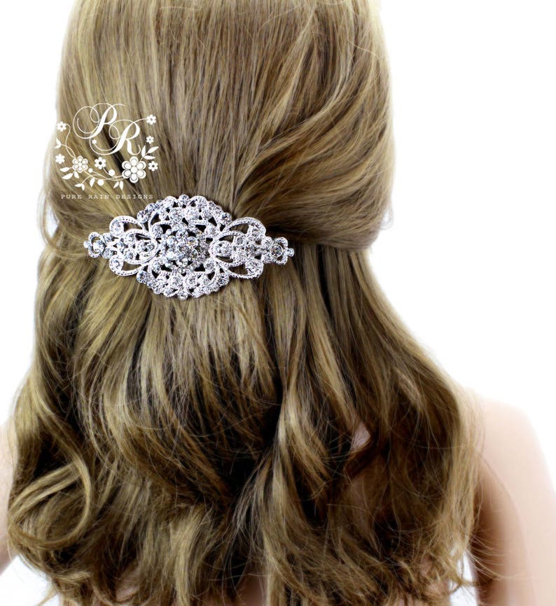 May include: A silver hair comb with a large, ornate design featuring clear rhinestones. The comb is shown in a model's hair.