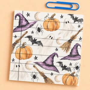 May include: A square notepad with horizontal lines featuring a watercolor pattern of purple witch hats, orange pumpkins, white ghosts, black bats, black spiders, crescent moons, and small black stars, accompanied by a blue paper clip.