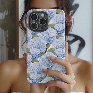 May include: A white phone case with a floral design featuring blue hydrangeas. The case has a camera lens cutout.