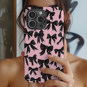 May include: A pink phone case with a black bow pattern. The case has a camera lens cutout and a black border.