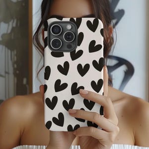 May include: A white phone case with a black heart pattern. The case has a camera lens cutout and a black border.