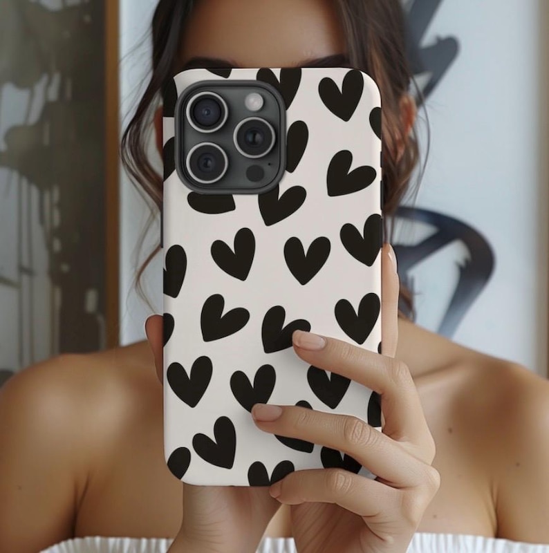 May include: A white phone case with a black heart pattern. The case has a camera lens cutout and a black border.