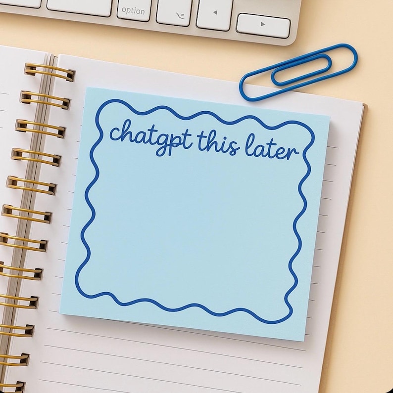 May include: A light blue sticky note with a wavy dark blue border and the text "chatgpt this later" in a handwritten style. The note is on a spiral notebook with a blue paperclip and a keyboard in the background.