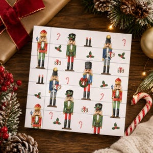 May include: A square white card featuring a repeating pattern of illustrated nutcrackers in red, green, and blue uniforms, interspersed with small gift boxes, holly sprigs, and candy canes arranged in a grid-like layout on a light background.