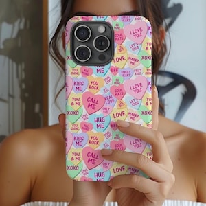 Op de afbeelding: Een roze, witte en blauwe telefoonhoes met een patroon van snoephartjes met daarop teksten als "Ik hou van je", "Kus me", "Bel me" en "Knuffel me".