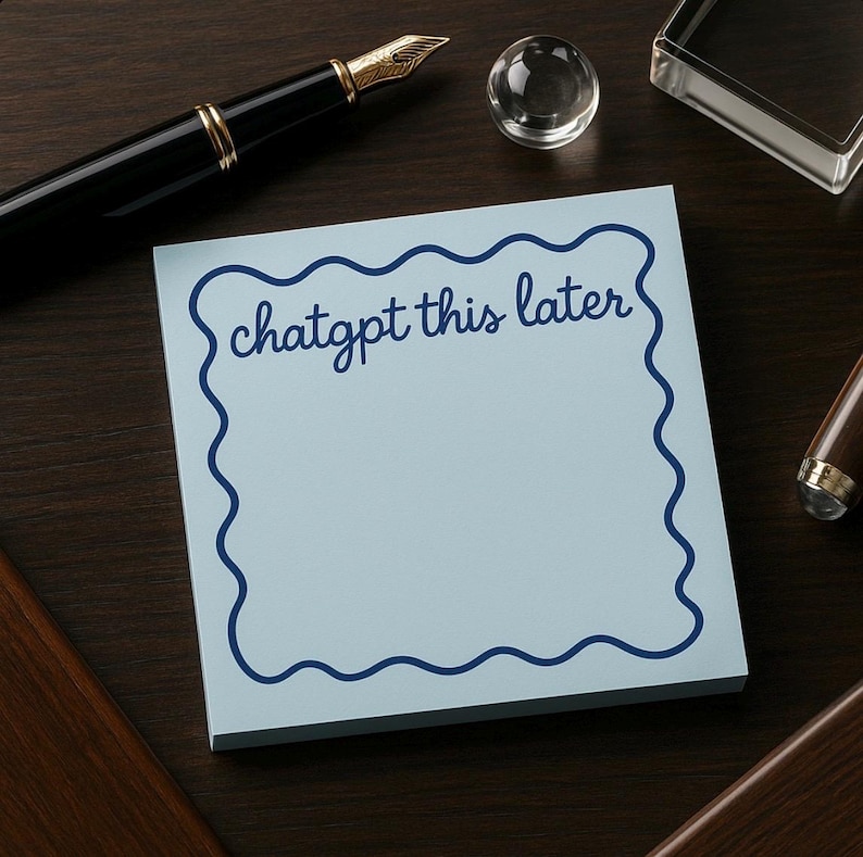 May include: A light blue sticky note pad with a wavy dark blue border and the words "chatgpt this later" in dark blue script. The pad is on a dark wood surface with a black pen and other desk accessories.