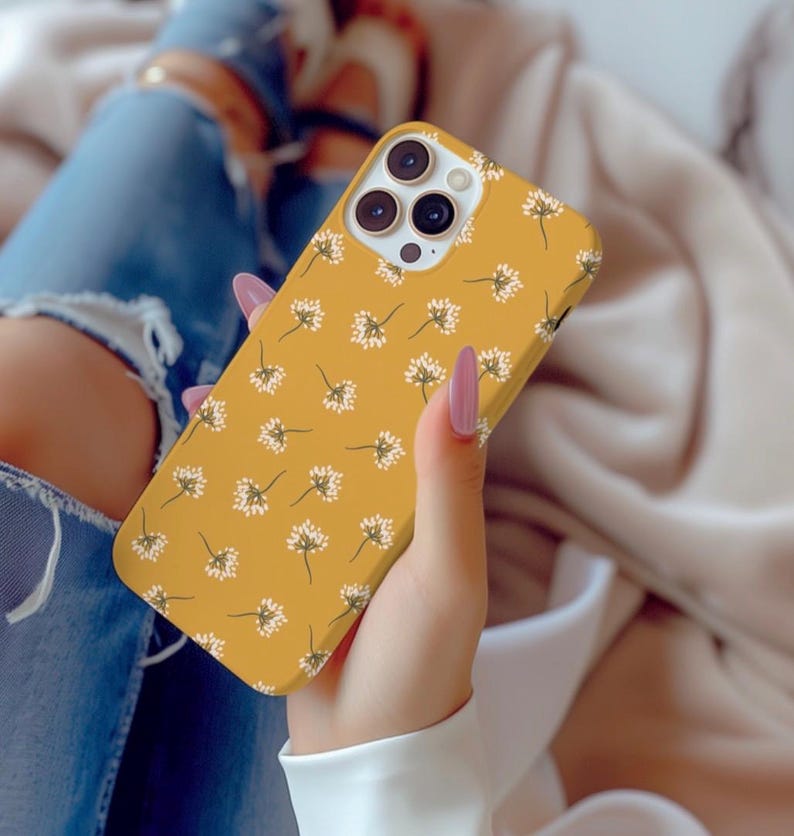 May include: A yellow phone case with a white floral pattern. The case has a camera lens cutout and a raised lip around the edges.